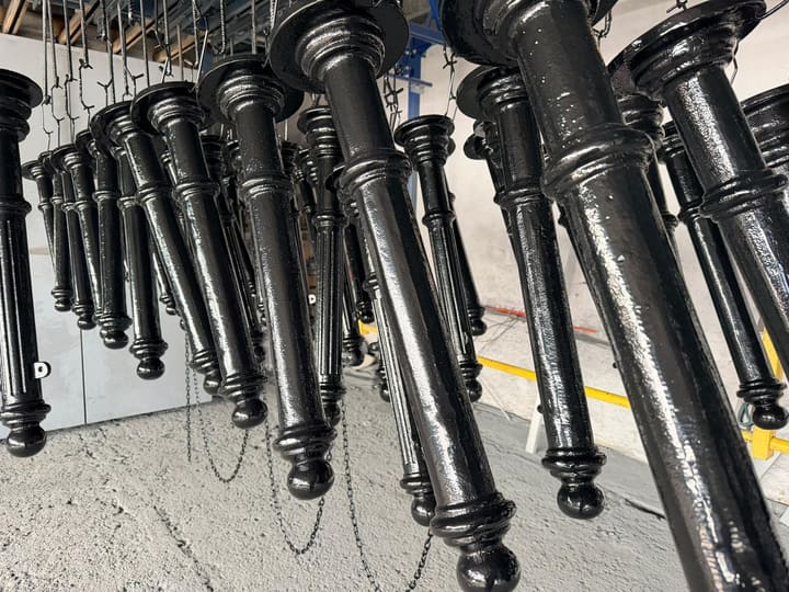 Czarne elementy balustrad zawieszone na linii lakierniczej